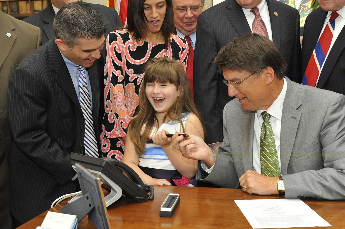 Governor McCrory hands Grace the pen at the signing of Senate Bill 98, with Eric Sanchez beside her